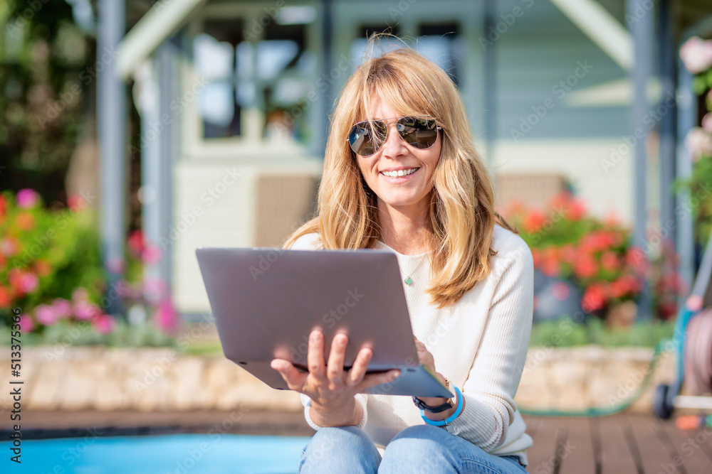 Confident middle aged woman using her laptop while relaxing at the backyard at home Confident middle aged woman using her laptop while relaxing at the backyard at home