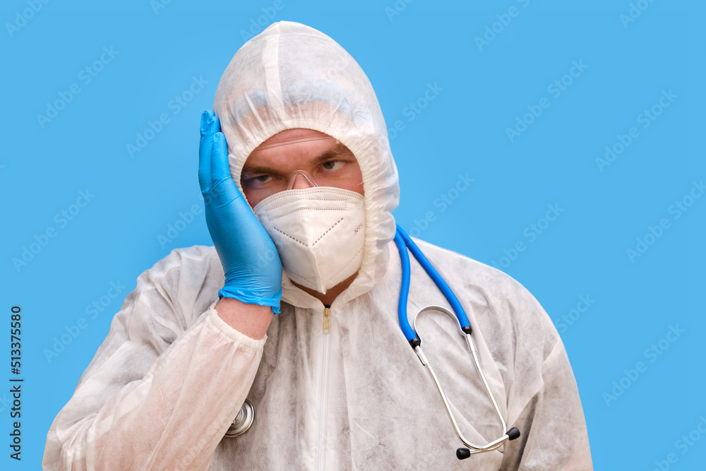 Man doctor medic in a protective suit uniform with goggles and face mask on a studio blue background. Paramedic in white antiviral protective clothing wearing an N95 respirator and safety glasses Man doctor medic in a protective suit uniform with goggles and face mask on a studio blue background. Paramedic in white antiviral protective clothing wearing an N95 respirator and safety glasses