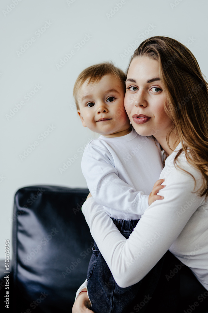 Young woman cuddling talking to small kid son, having fun together on couch in studio living room. Smiling child boy communicating with elder sister nanny babysitter, laughing at home. Young woman cuddling talking to small kid son, having fun together on couch in studio living room. Smiling child boy communicating with elder sister nanny babysitter, laughing at home.
