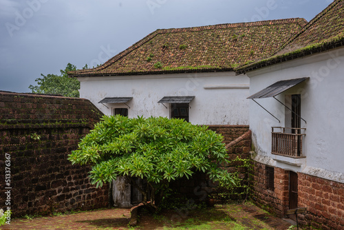 Interiors of a fort in Goa which shows the building architecture of Portuguese colonial influence having laterite stones, windows, doors and tiled roofs with the Monsoon sky in background