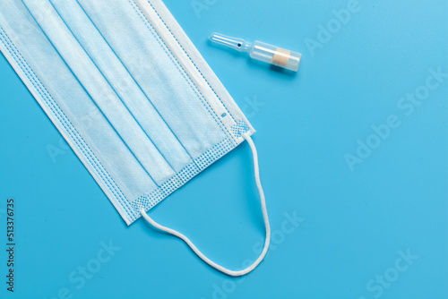 Medical mask. Blue medical mask and ampoule with white liquid, isolated on blue background.