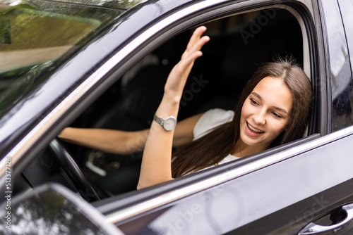 say hello. Beautiful happy woman sits in the car and waving his hand in greeting