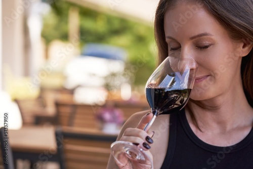 Close up portrait of beautiful young woman tasting red wine, holding wineglass.