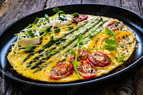 Tasty breakfast. Omelette  with green asparagus, goat cheese, pepper and cherry tomatoes served on black plate on wooden table

