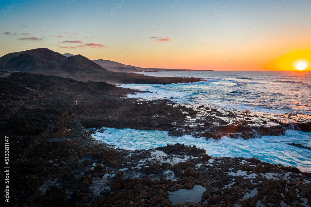 aerial view of sun setting behind blue ocean with mountains on coastline on lanzarote