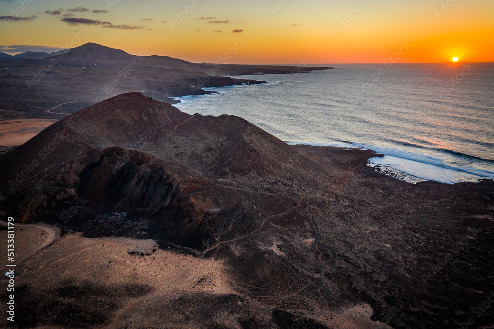 aerial view of sunset above ocean with volcanos and mountains on coastline