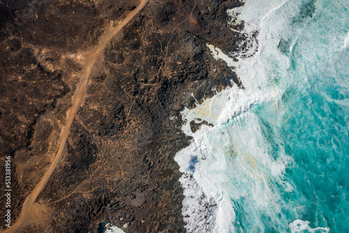 aerial view of hiking trail and ocean waves breaking on rocky coast 