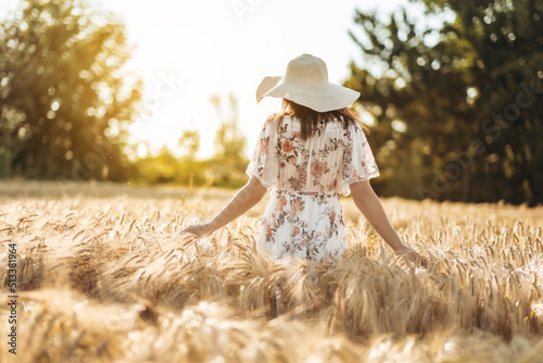 a woman in a sundress walks through a wheat field at sunset