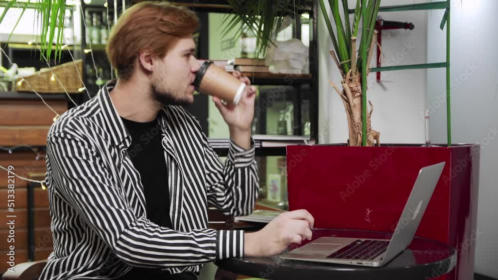 Close-up of a guy sitting in a cafe with a laptop at a table, drinking coffee and talking via video link. Working outside the home Close-up of a guy sitting in a cafe with a laptop at a table, drinking coffee and talking via video link. Working outside the home