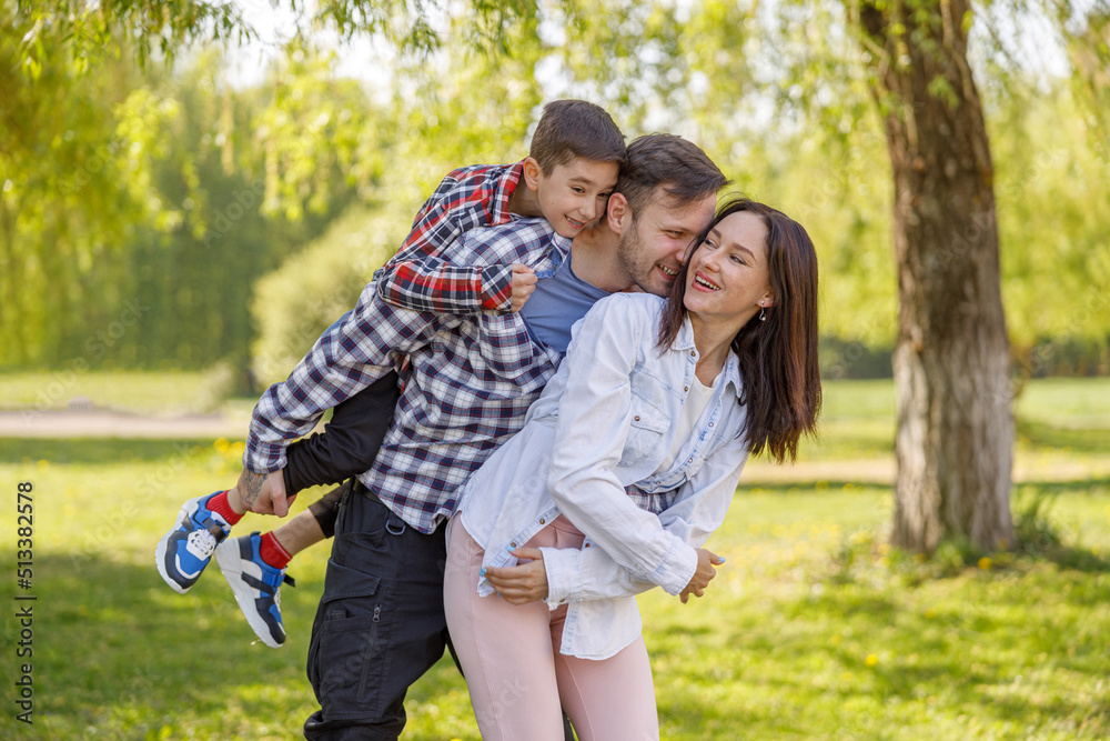 Fototapeta premium Portrait of happy Caucasian family in green summer park. Parents with son hugging in live.