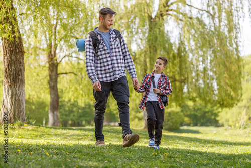 Caucasian father and little son with backpack walking the park or forest on summer day.