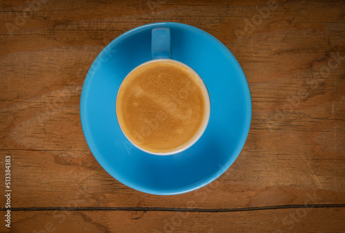 Fresh coffee in blue cup on dirty old wooden table from above