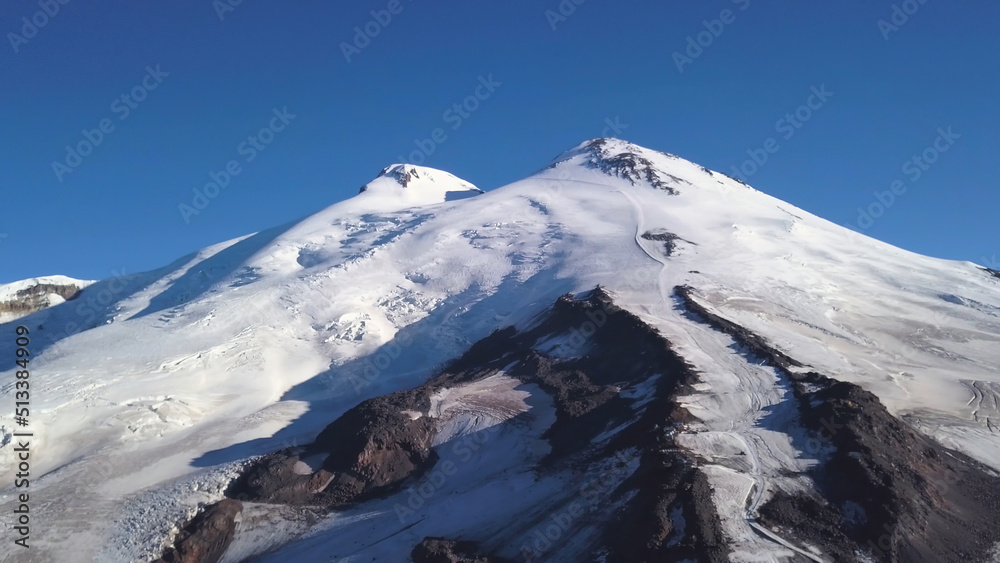 Snowy and icy mountain peaks of glaciers in Austrian Alps at winter. Clip. Aerial view of a snowy slope of a huge rock on blue sky background.