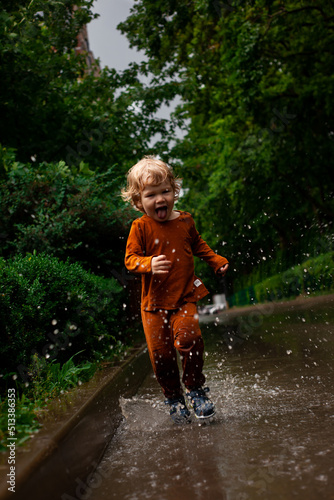 Fototapeta Naklejka Na Ścianę i Meble -  a little boy runs and jumps in the puddles during the summer rain.Childhood.