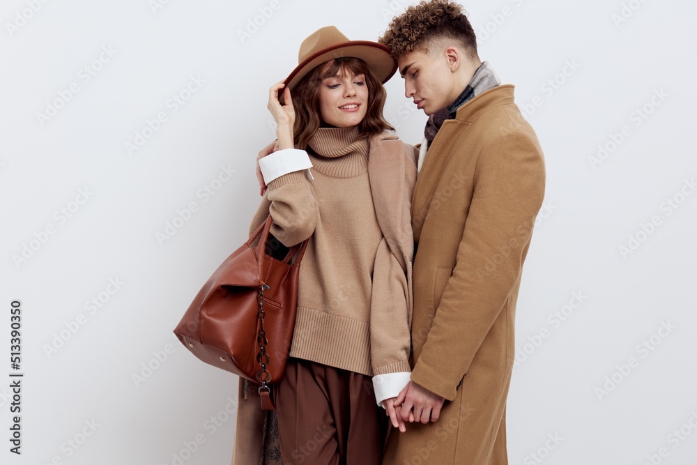 beautiful couple in love is standing on a white background in autumn clothes and holding hands sweetly, and a man looks lovingly at a woman, putting his arm around her shoulder, she has an autumn hat beautiful couple in love is standing on a white background in autumn clothes and holding hands sweetly, and a man looks lovingly at a woman, putting his arm around her shoulder, she has an autumn hat