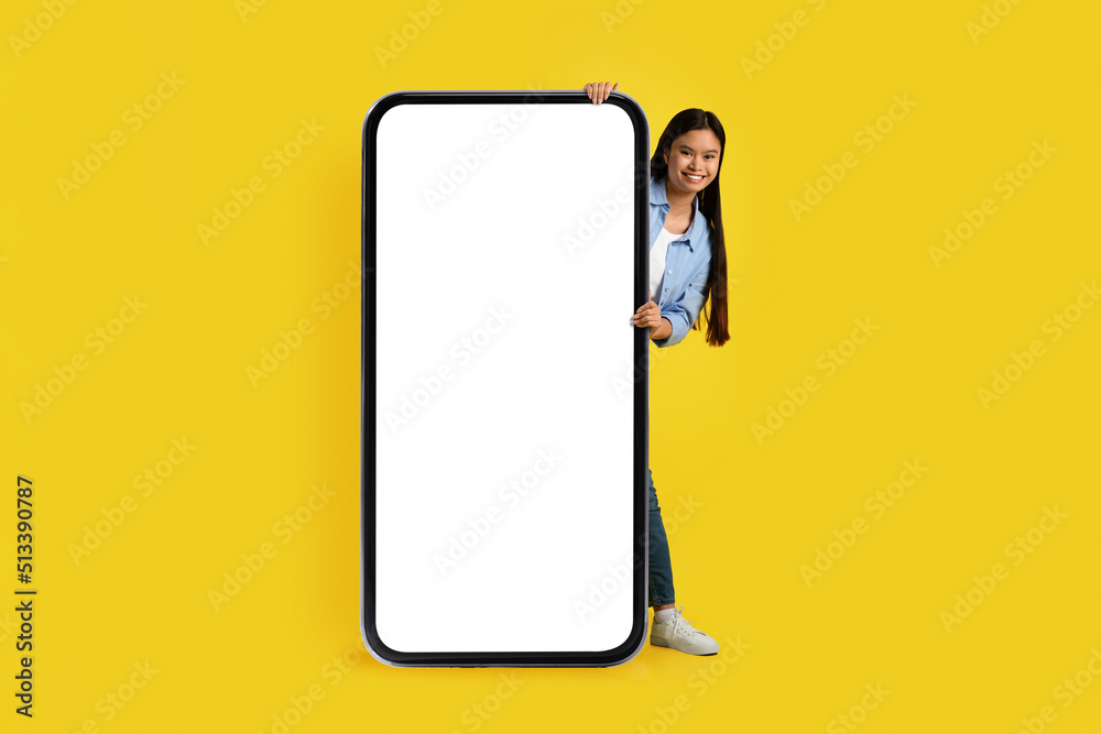 Glad funny young korean female peeking out from behind huge phone with blank screen Glad funny young korean female peeking out from behind huge phone with blank screen