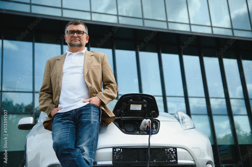 Casual man near electric car waiting for the finish of the battery charging process. Casual man near electric car waiting for the finish of the battery charging process.