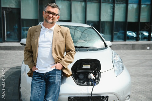 Casual man near electric car waiting for the finish of the battery charging process. © Serhii