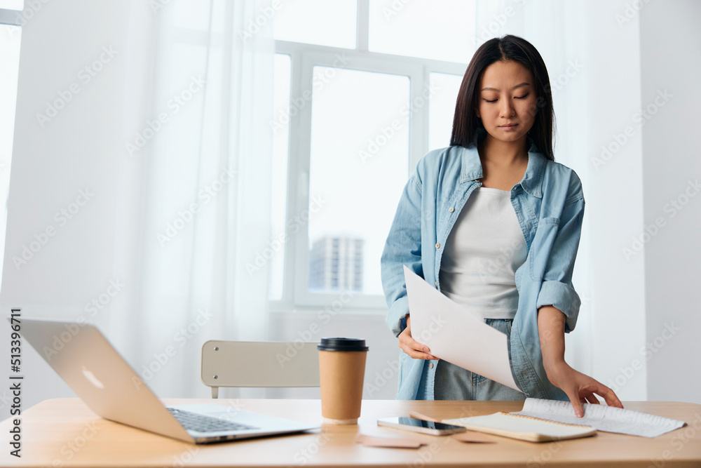 Concentrated thoughtful young Asian cute female businesswoman deals with documents on table with laptop in office interior. Employee work at home. Lady corporation leader concept. Copy space Offer