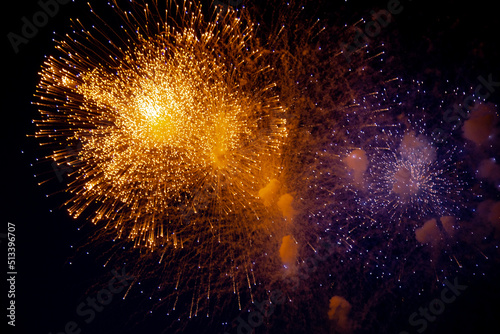 A bright orange firework and next to it a blue firework with sparks on the background of the night sky. High quality photo
