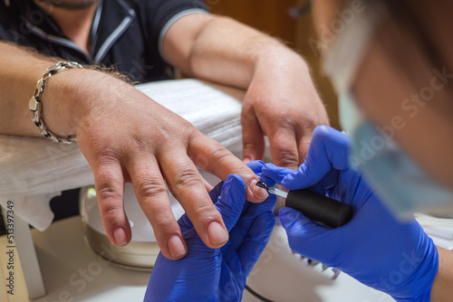 manicure master paints the man clients nails with gel polish in a beauty salon. Manicure male service close up