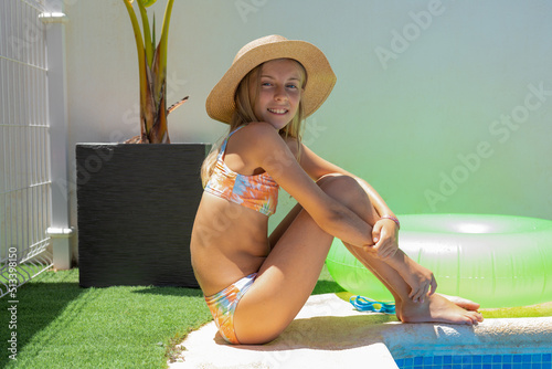 Pretty young girl in straw hat lying near the pool. Summertime concept.