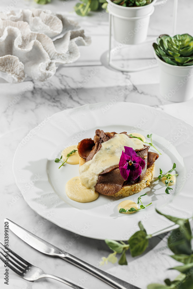 Baked sliced beef tongue delicatesse on a rice garnish with cream sauce at the white plate on light marble background. Healthy sea food, hard light, restaurant decor, close up