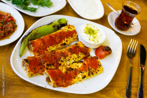 Traditional Turkish beyti sarma from grilled ground beef wrapped in flat bread topped with spicy tomato sauce 