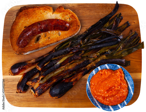 Traditional dishes of Catalonia, calcot with romesco sauce and grilled botifarra sausage served on wooden board. Isolated over white background photo