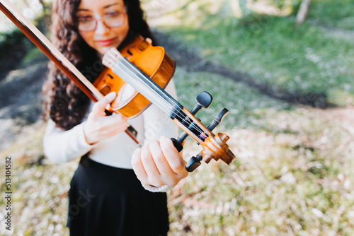 Curly brunette woman with glasses tuning her violin outside in the woods. Copy space