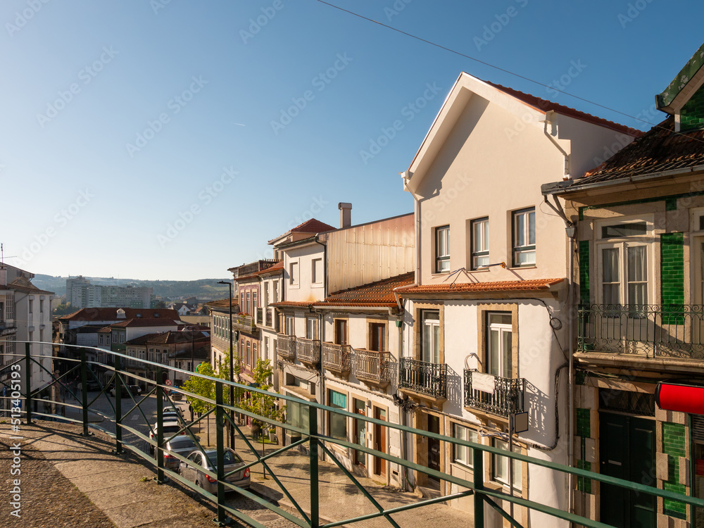 View of empty narrow street in Portuguese city of Vila Real with townhouses decorated with forged balconies on sunny spring day .