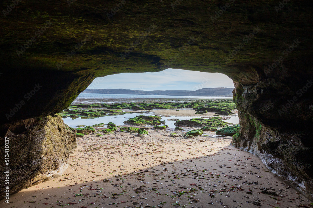 View from the cave to the sandy beach, huge stones with algae during the low tide of the Atlantic Ocean, Valdes Peninsula, Puerto Piramides, Patagonia, Argentina