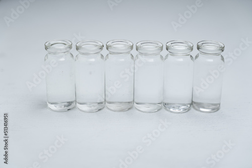 hilera de 6 botellas pequeñas de vidrio sobre fondo con textura claro, llenos de agua, simple y limpio.
