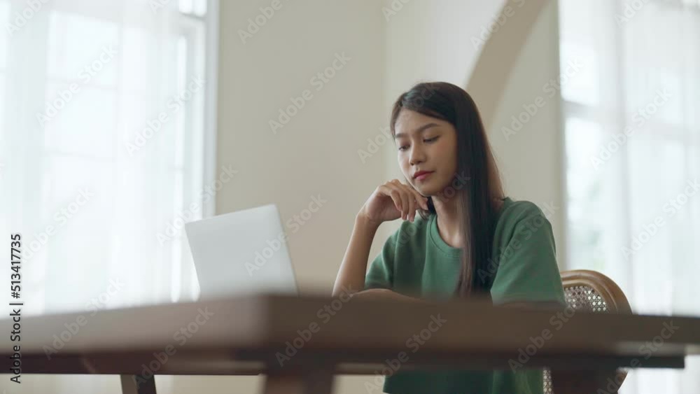 Asian young woman seriously working on computer laptop in house. She thinking find solution problem of work Asian young woman seriously working on computer laptop in house. She thinking find solution problem of work