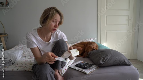 Frustrated middle-aged woman worrying about unpaid bills and rising cost of living, sitting on sofa with dog at home, upset unemployed lady holding invoice receipts feeling anxious about finances photo