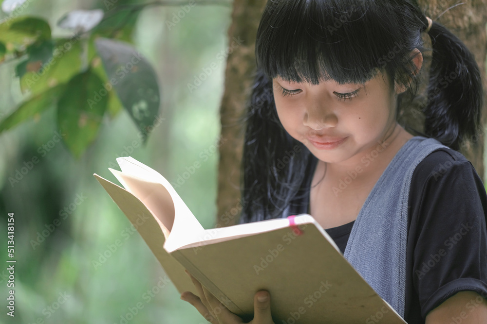 Fototapeta premium Child little girl reading read book in park under tree.