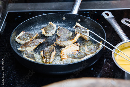 Pieces of fish cooking on a hot pan with olive oil on a stove. Dinner