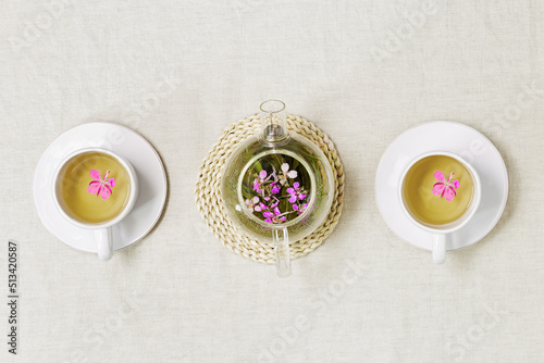 Herbal tea from kipreya leaves in white cups on linen fabric table background, fireweed green leaves and flowers on wooden tray. Flavored herbal tea from natural plants, healing hot beverage.