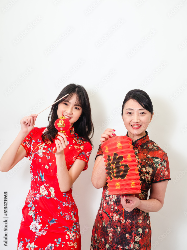 Portrait of young asian woman and elder woman both wearing traditional cheongsam qipao dress hold red paper lantern with word meaning good fortune and treasure on white background. Portrait of young asian woman and elder woman both wearing traditional cheongsam qipao dress hold red paper lantern with word meaning good fortune and treasure on white background.