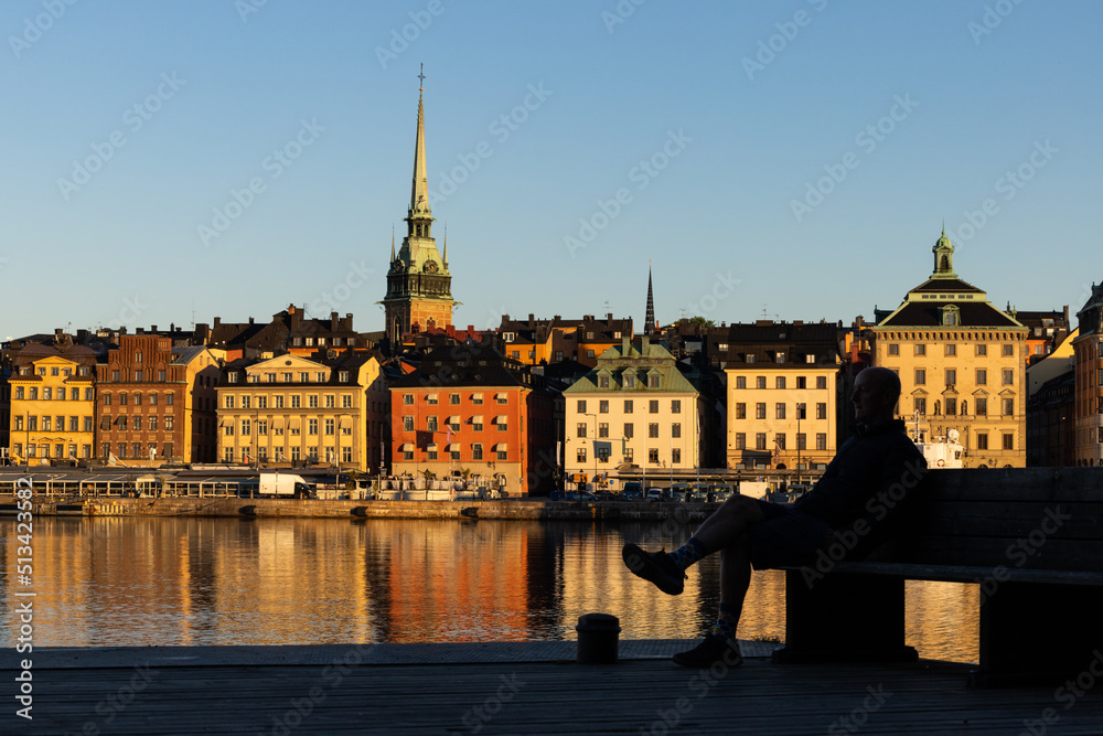 Stockholm, Sweden A man sits on a bench on Skeppsholmen with a view over water and Gamla Stan, or Old Town.