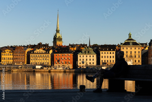 Stockholm, Sweden A man sits on a bench on Skeppsholmen with a view over water and Gamla Stan, or Old Town.