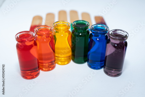 hilera de botellitas con agua coloreada multicolor, arcoiris con fondo blanco y palitos de madera en la base