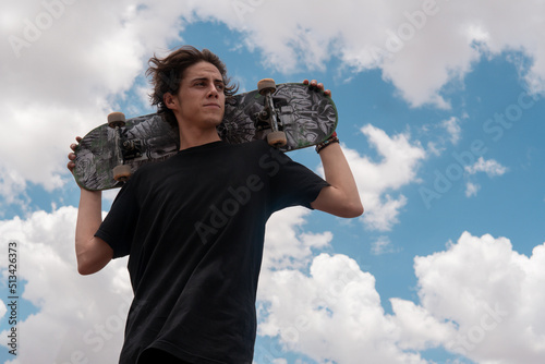 Young guy in a black t-shirt posing with his skateboard on his shoulders