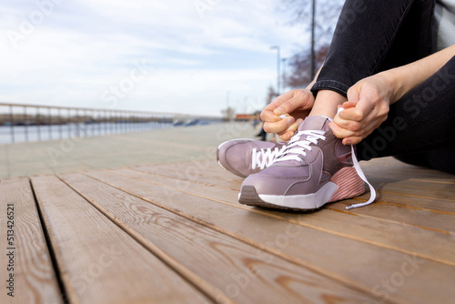 woman sits on a wooden platform and ties her shoelaces on her sneakers