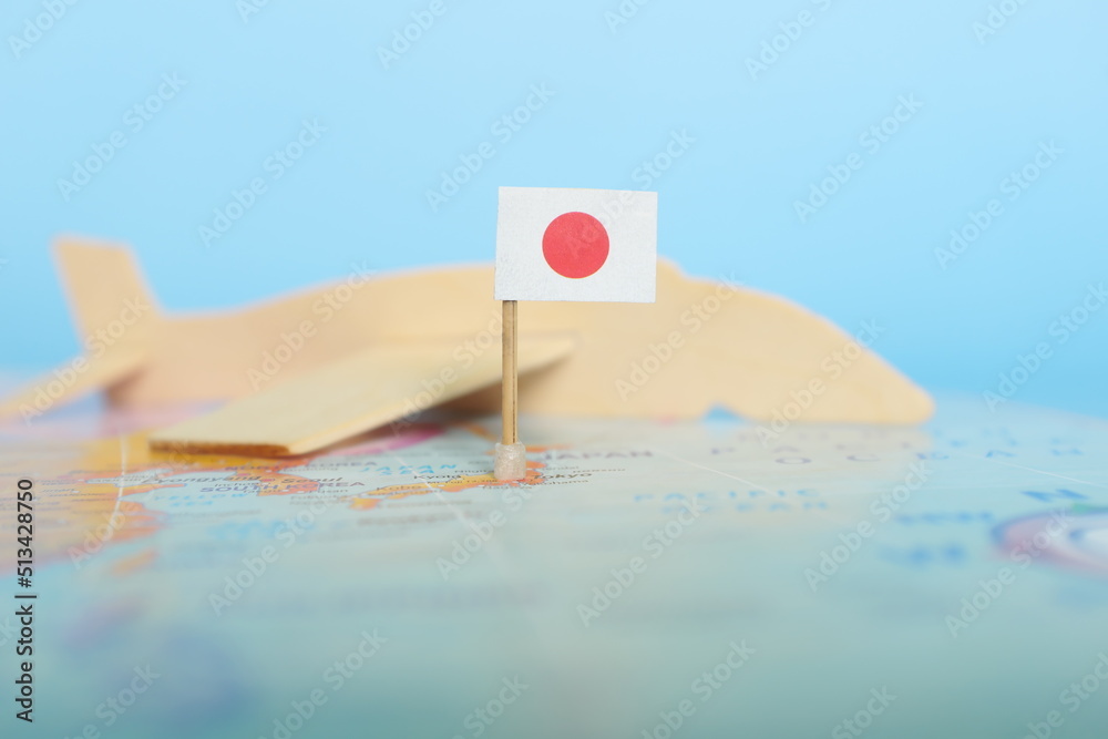 Selective focus of Japanese flag in blurry world map and wooden airplane model. Japan as travel and tourism destination concept.	
