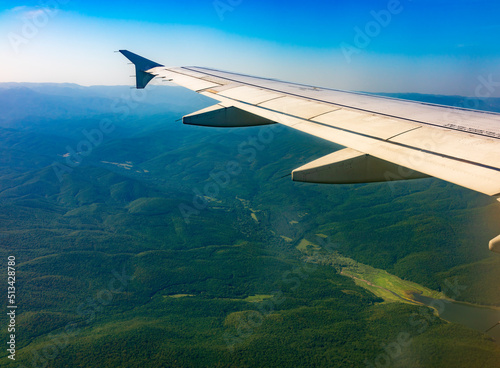 View of airplane wing, blue skies and green land during landing. Airplane window view.