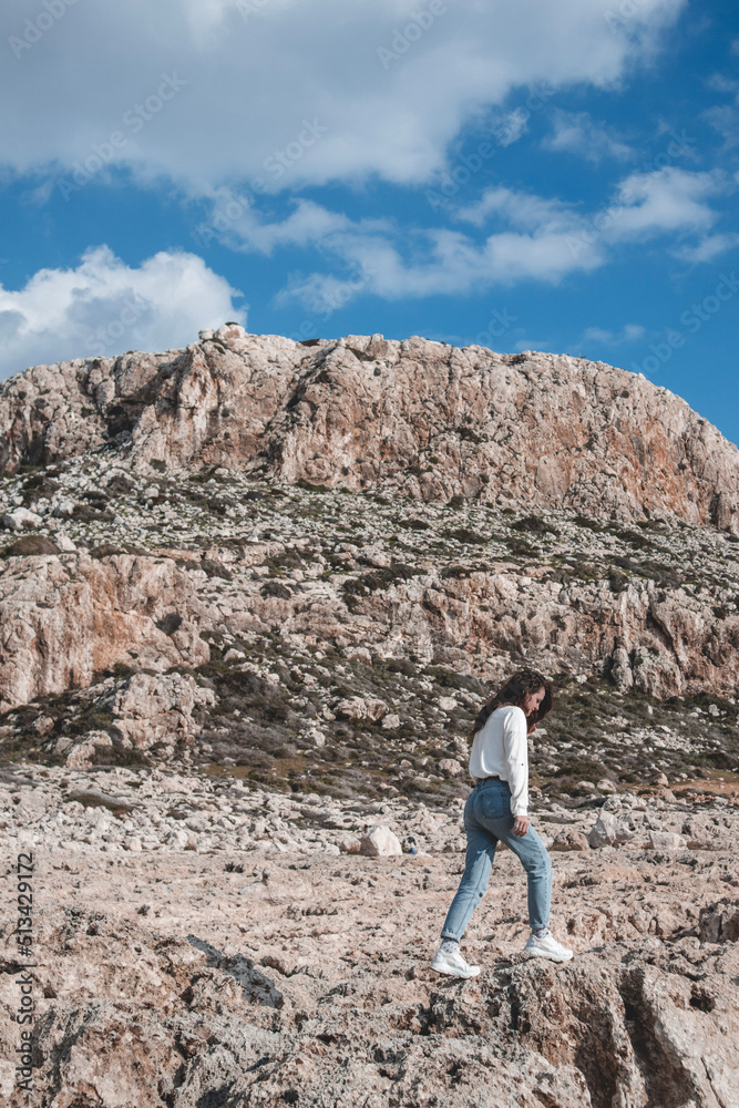 Young woman is jumping in a desert ground in front of the mountain Cape Greco