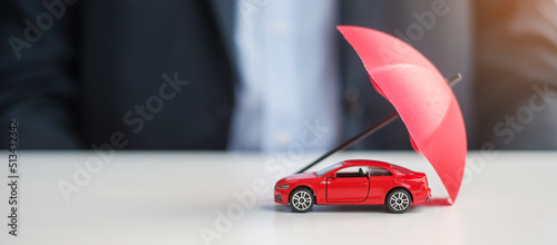 Businessman hand holding umbrella and cover  red car toy on table. Car insurance, warranty, repair, Financial, banking and money concept