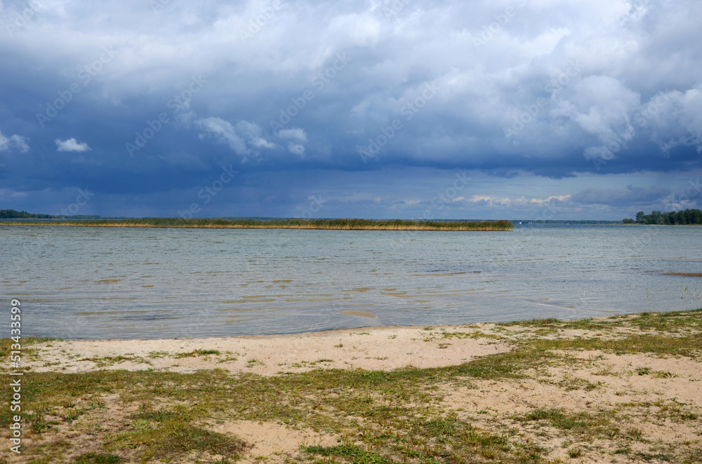  Landscape with lake coast and dramatic sky with clouds over the water before  incoming rain and thunderstorm.