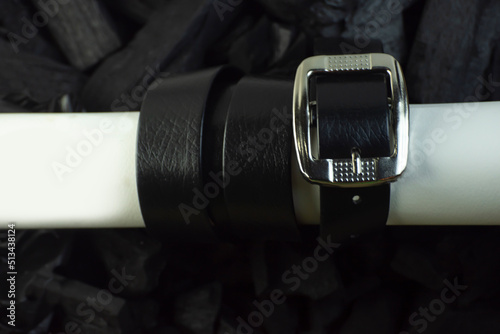 Waist belt, black leather, rolled on white paper. on a dark charcoal background, blur